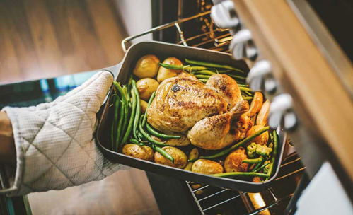 Person with oven mittens on retrieving roast chicken from the oven