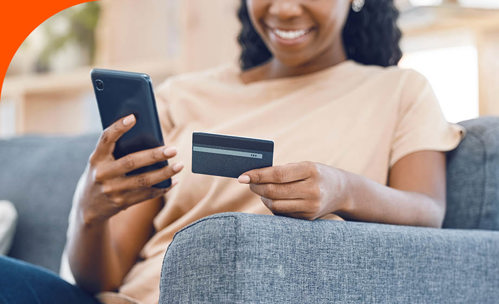 Woman smiling while using her smartphone and holding a card in her other hand.